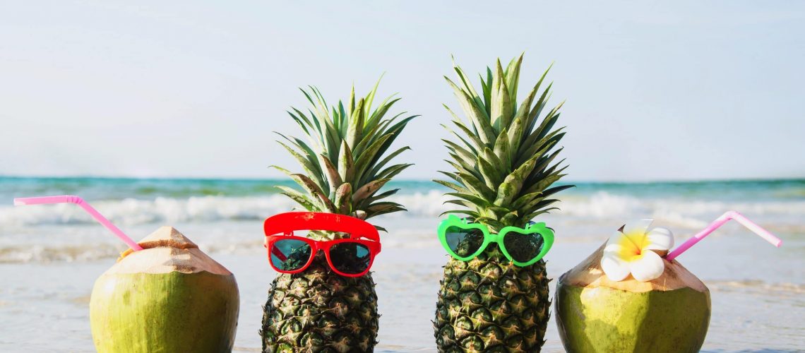 Fresh coconut and pineapple put sun lovely glasses on clean sand beach with sea wave background - fresh fruit with sea sand sun vacation background concept
