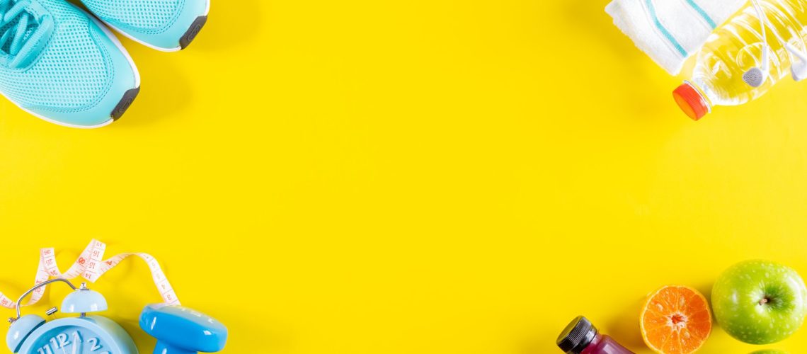 Healthy lifestyle, food and sport concept. Fitness equipment. Sneakers, water, dumbbells and headphones on yellow background.