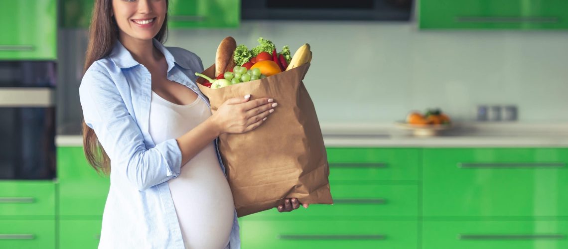 Beautiful pregnant woman is holding a paper bag with food.