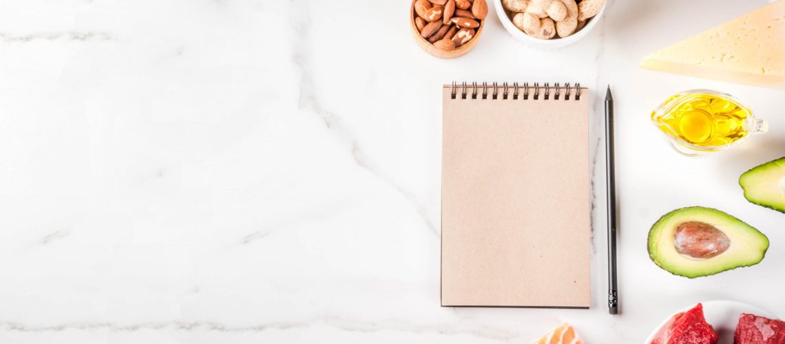 Ketogenic low carbs diet concept. Healthy balanced food with high content of healthy fats. Diet for the heart and blood vessels. Organic ingredients, white background, copy space top view, notepad